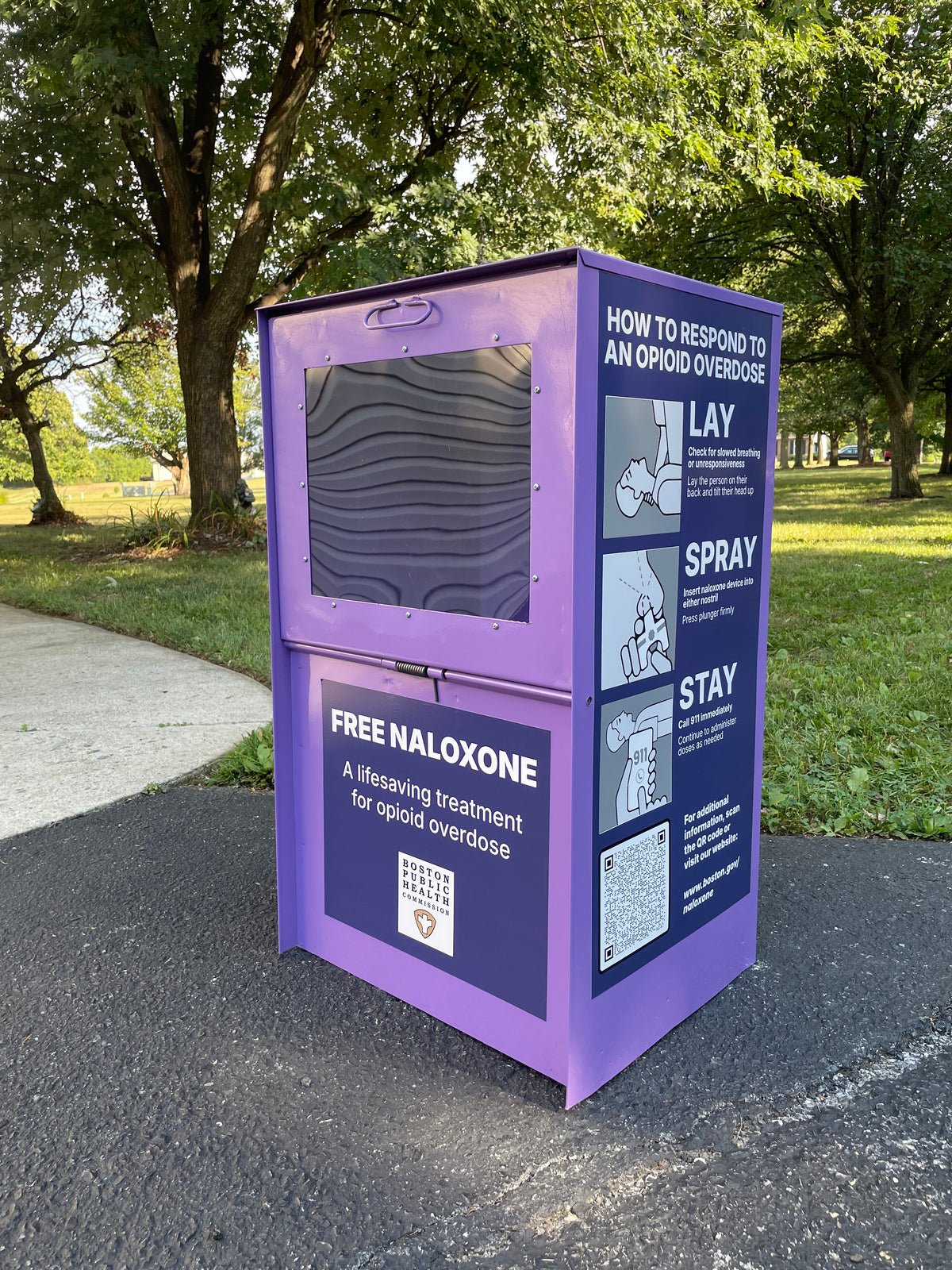 Purple steel weather-proof Narcan dispenser kiosk about naloxone in a park setting