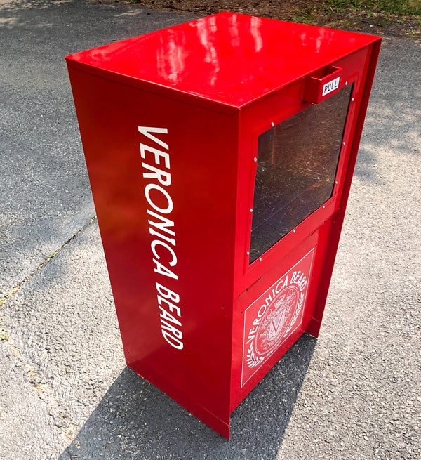 Red vending machine with 'Veronica Beard' branding on a concrete surface.